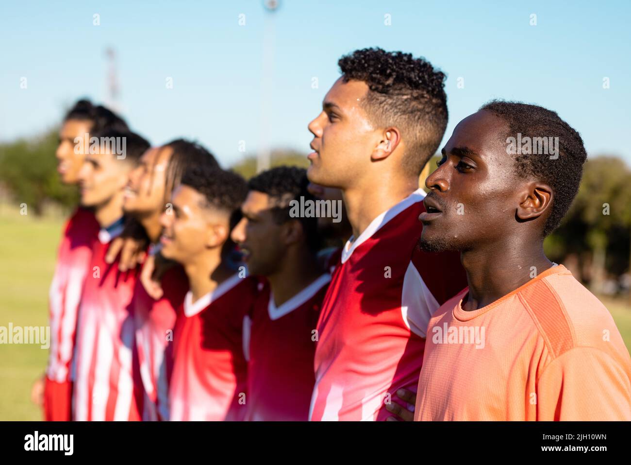 Multiracial male players in red uniforms looking away and standing side by side against clear sky Stock Photo