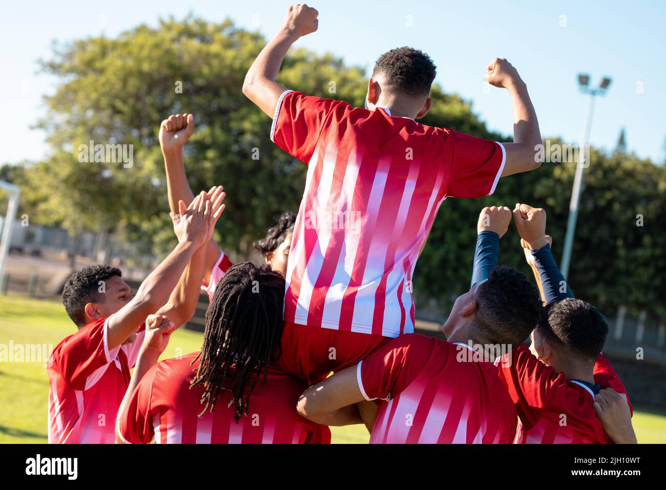 Rear view of multiracial cheerful players carrying teammate on shoulders while celebrating goal Stock Photo