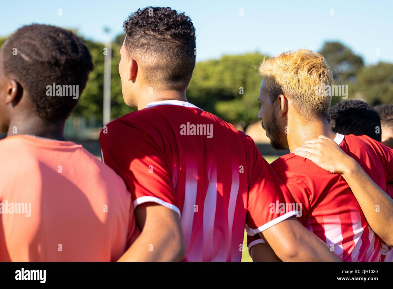 Rear view of multiracial male players in uniforms with arms around standing side by side Stock Photo