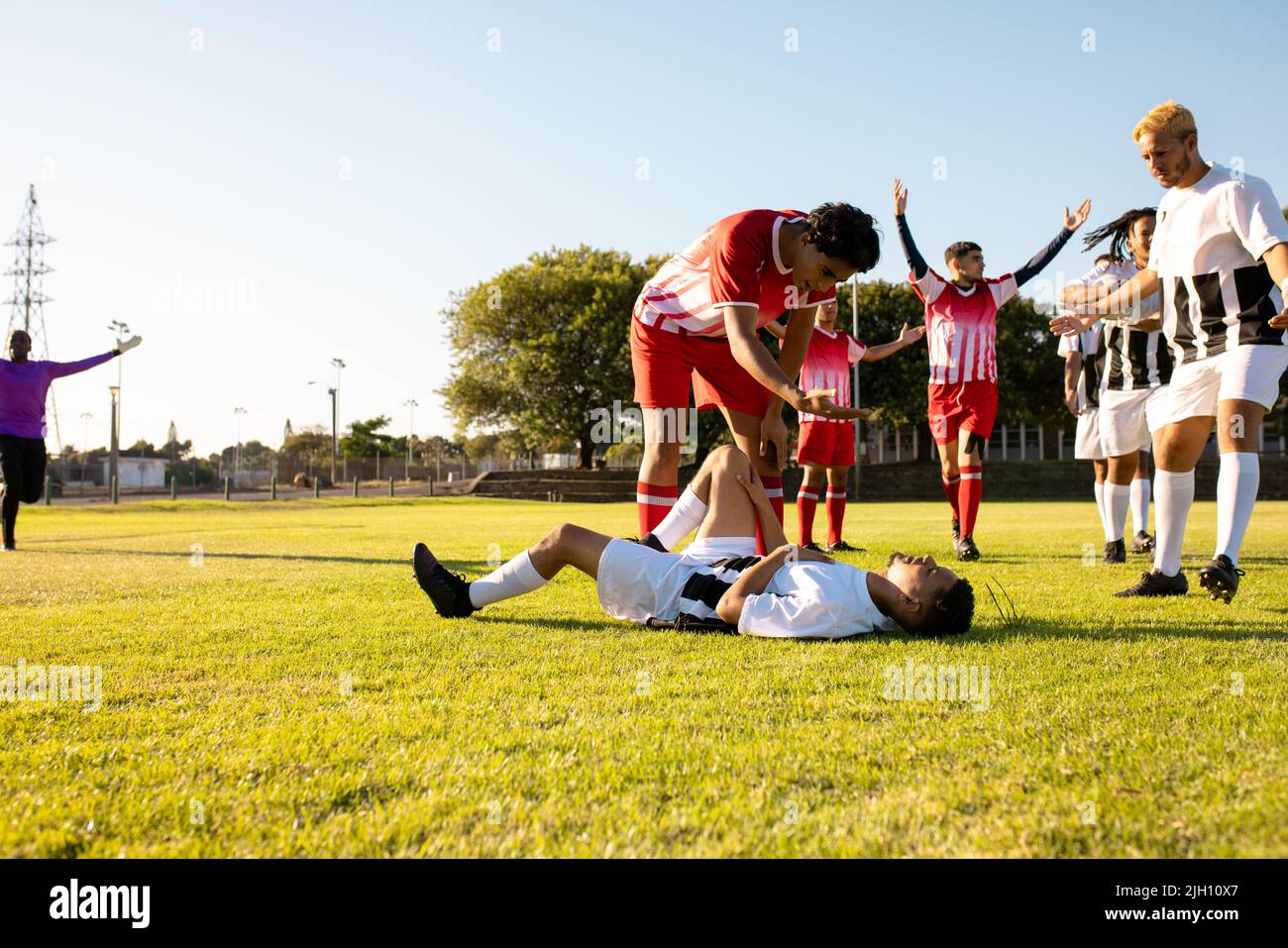 Multiracial male soccer teams running towards injured player lying on grassy field during match Stock Photo