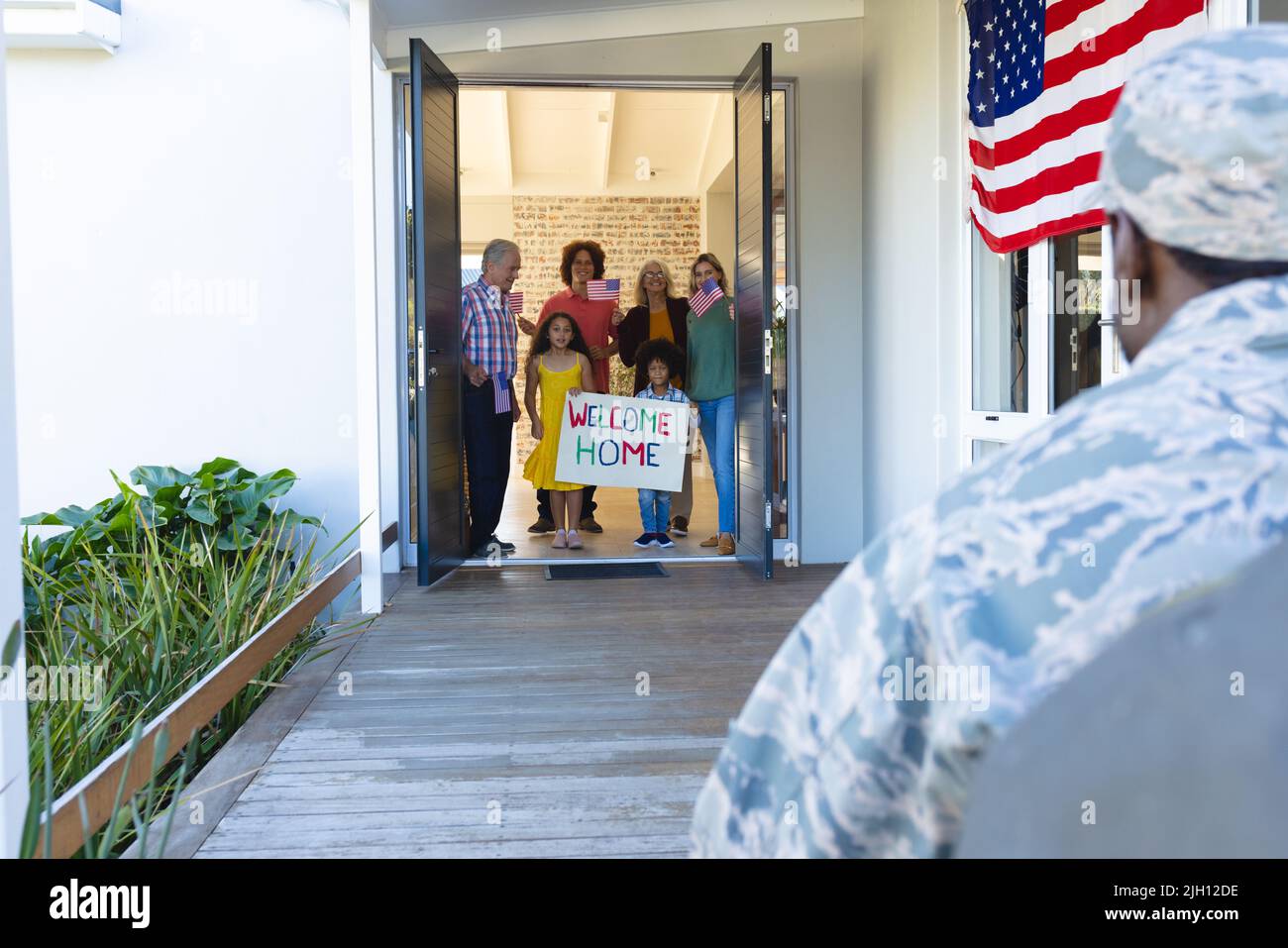 Multiracial soldier coming home and multigeneration family with flags welcoming him at entrance Stock Photo