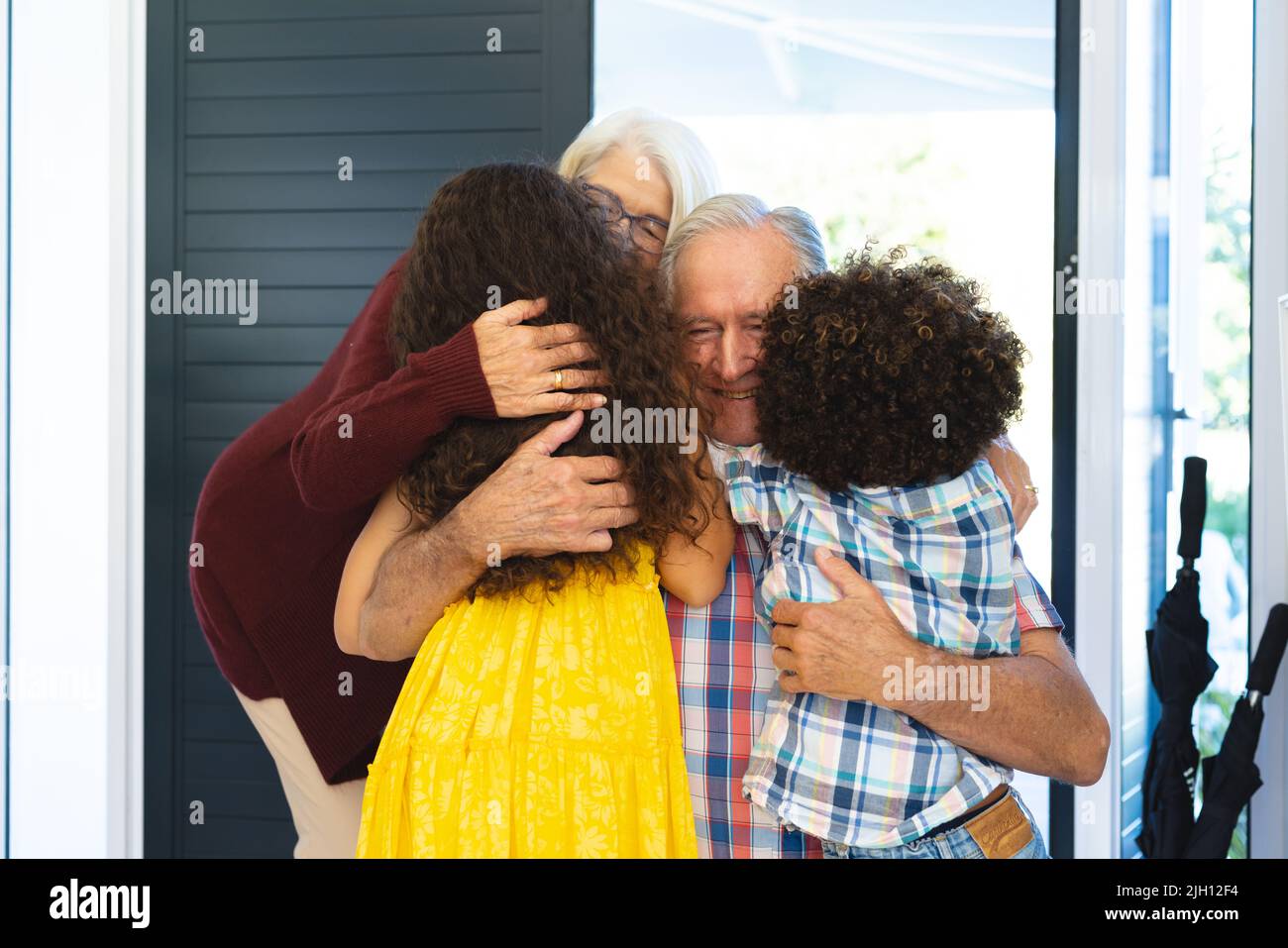 Multiracial grandchildren embracing grandparents while welcoming them at home at entrance Stock Photo