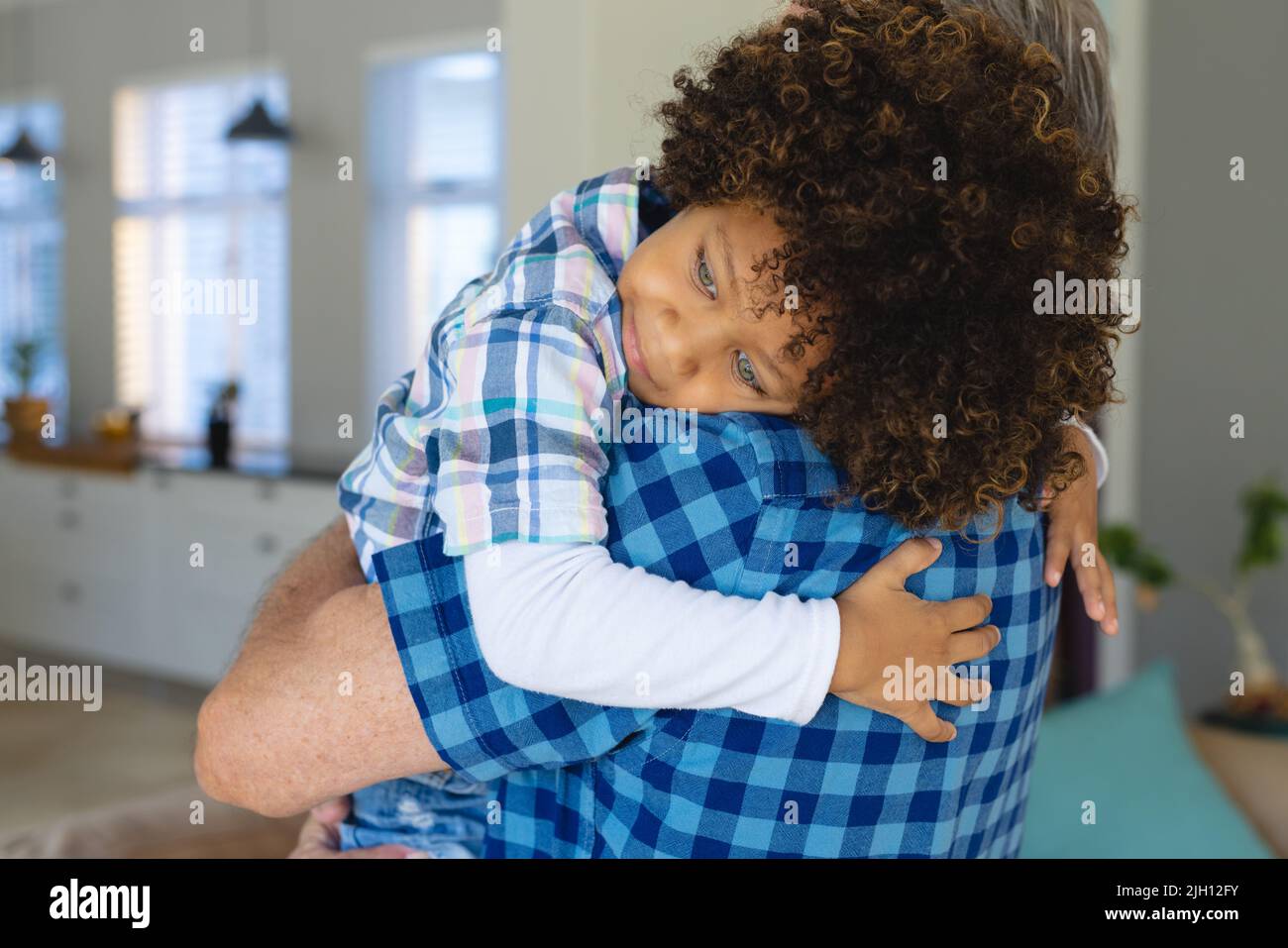 Caucasian grandfather carrying cute biracial grandson with afro hair while standing at home Stock Photo