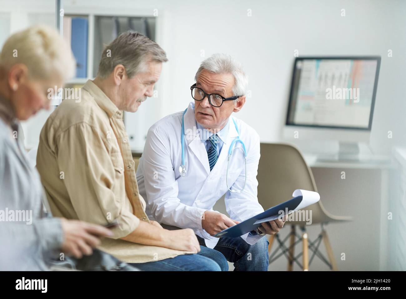 Serious senior male doctor in white coat and eyeglasses holding