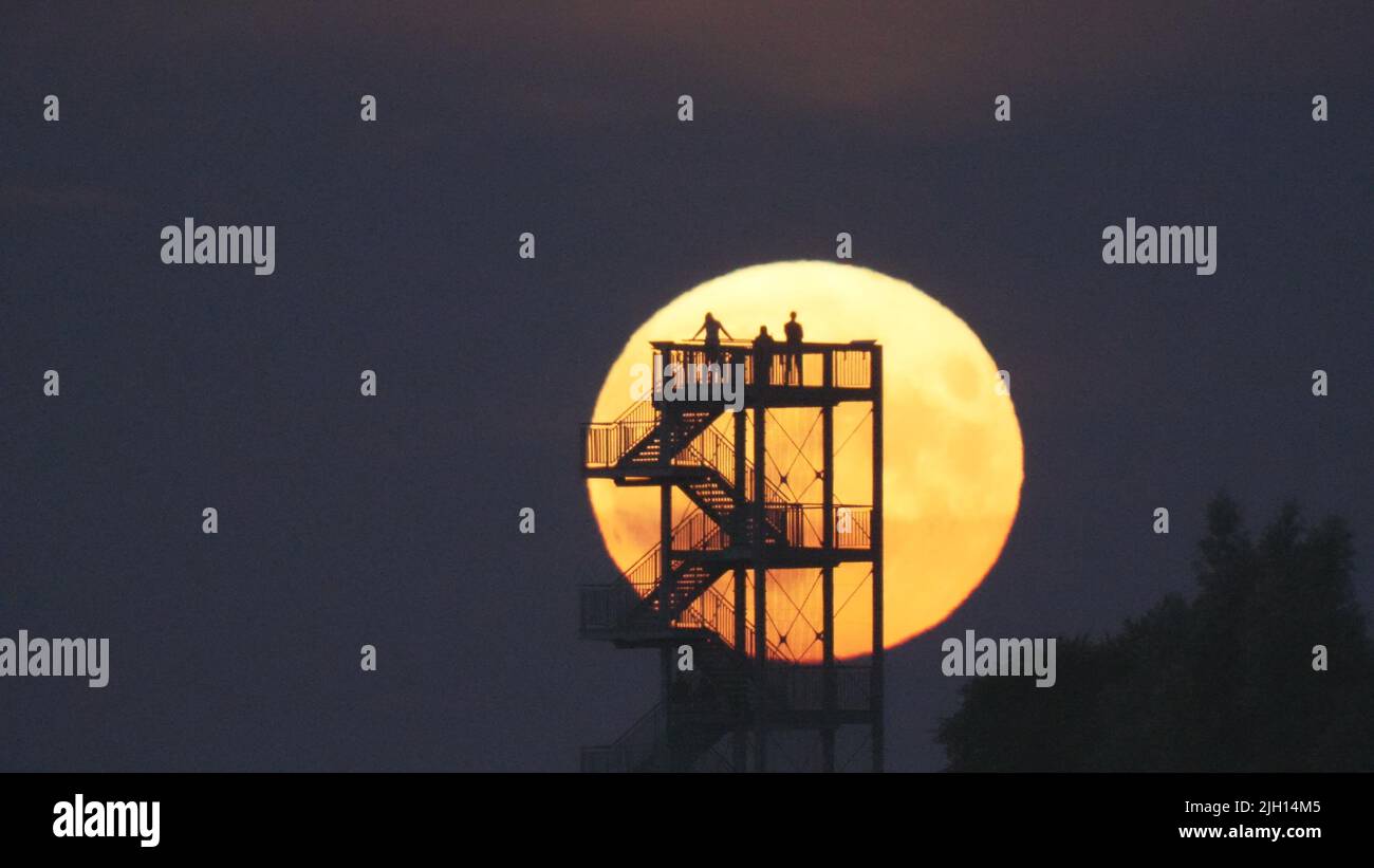 Syke, Germany. 14th July, 2022. Onlookers watch the moonrise from the observation tower on the Hohe Berg. The so-called supermoon is a celestial event that occurred for the second time within a few weeks. The earth's satellite then appears somewhat larger than usual. The moon looks particularly impressive directly after rising and shortly before setting. Credit: Thomas Lindemann/dpa/Alamy Live News Stock Photo