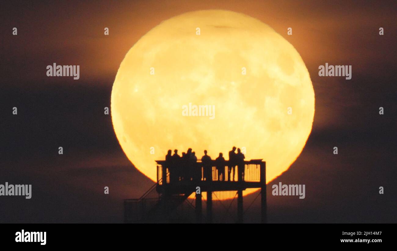 Syke, Germany. 14th July, 2022. Onlookers watch the moon rise from the observation tower on the Hohe Berg. The so-called supermoon is a celestial event that occurred for the second time within a few weeks. The earth's satellite then appears somewhat larger than usual. The moon looks particularly impressive directly after rising and shortly before setting. Credit: Thomas Lindemann/dpa/Alamy Live News Stock Photo