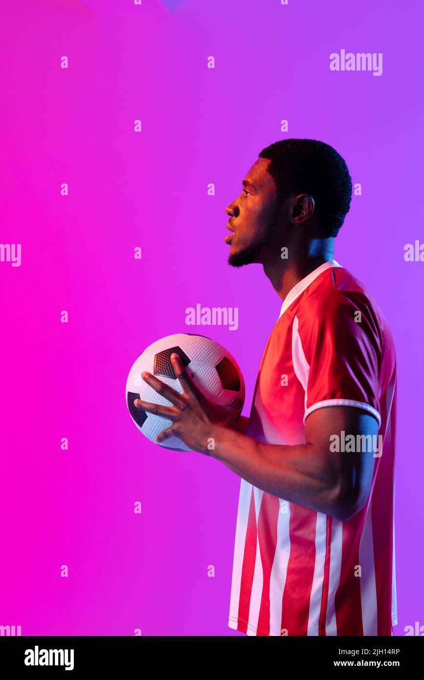 African american male soccer player with football over neon pink