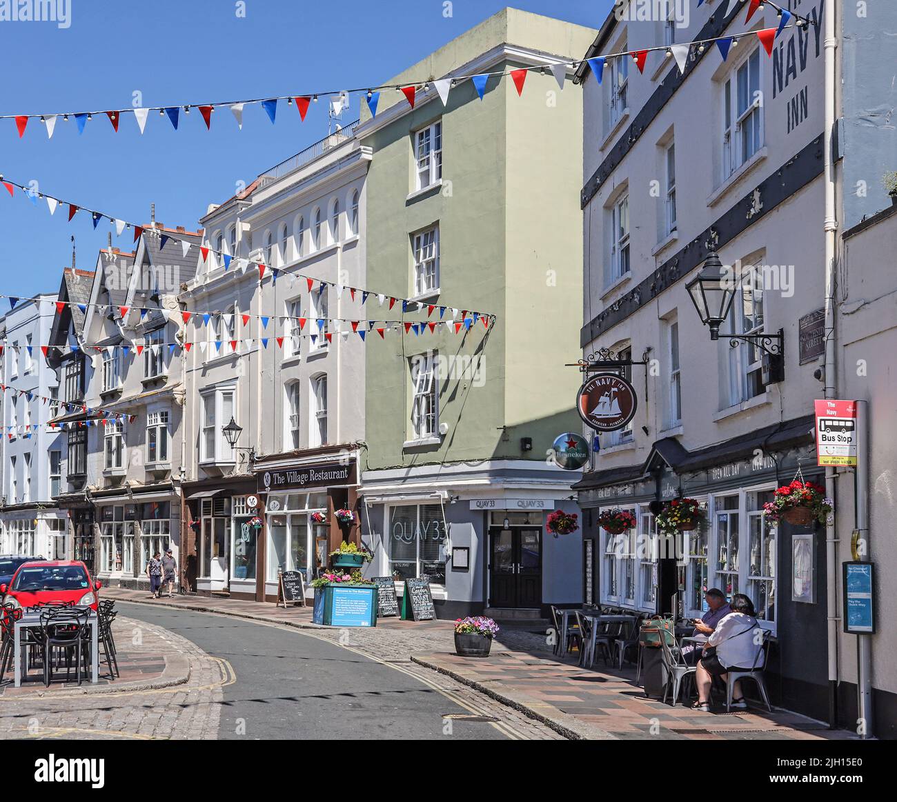 Flower tubs and bunting add colour to Southside Street on Plymouth’s historic Barbican on a quiet Sunday morning. A quirky mix of small shops, public Stock Photo
