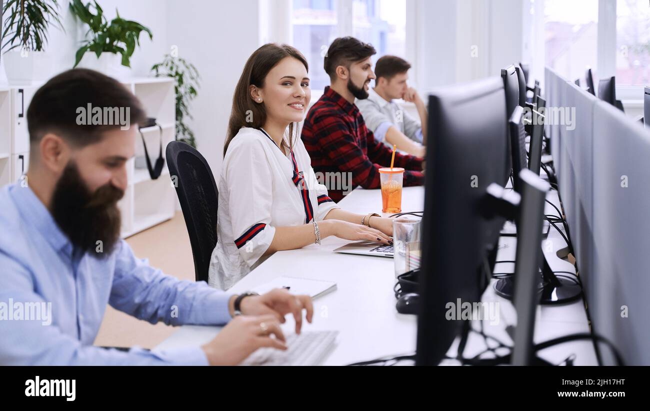 Junior female professional working in modern IT office. Group of young and experienced programmers and software developers sitting at desks working on Stock Photo