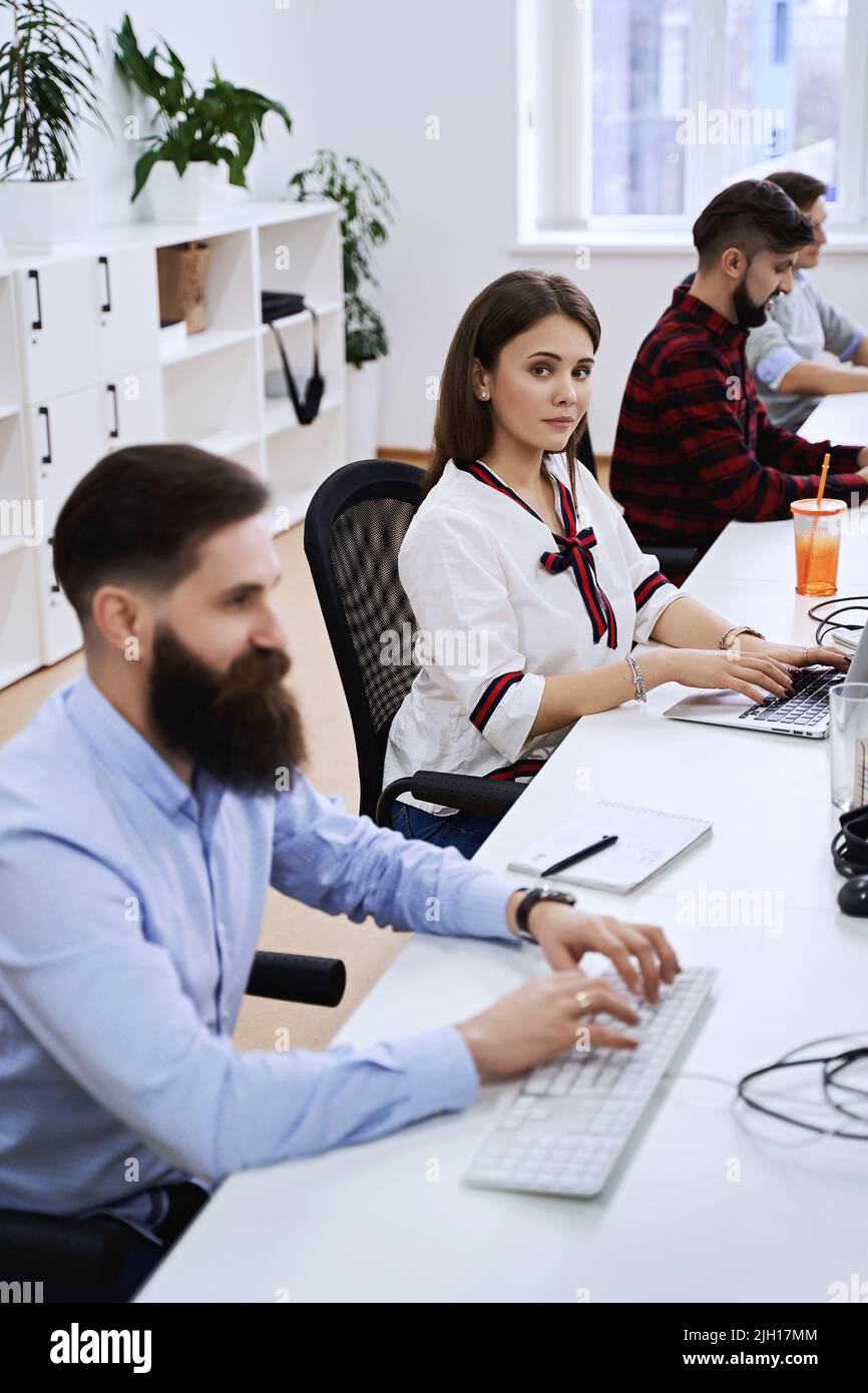 People working in modern IT office. Group of young and experienced programmers and software developers sitting at desks working on computers. Team at Stock Photo