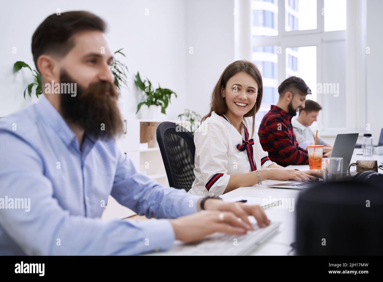 People communicating and working in modern IT office. Group of young and experienced programmers and software developers sitting at desks working on Stock Photo