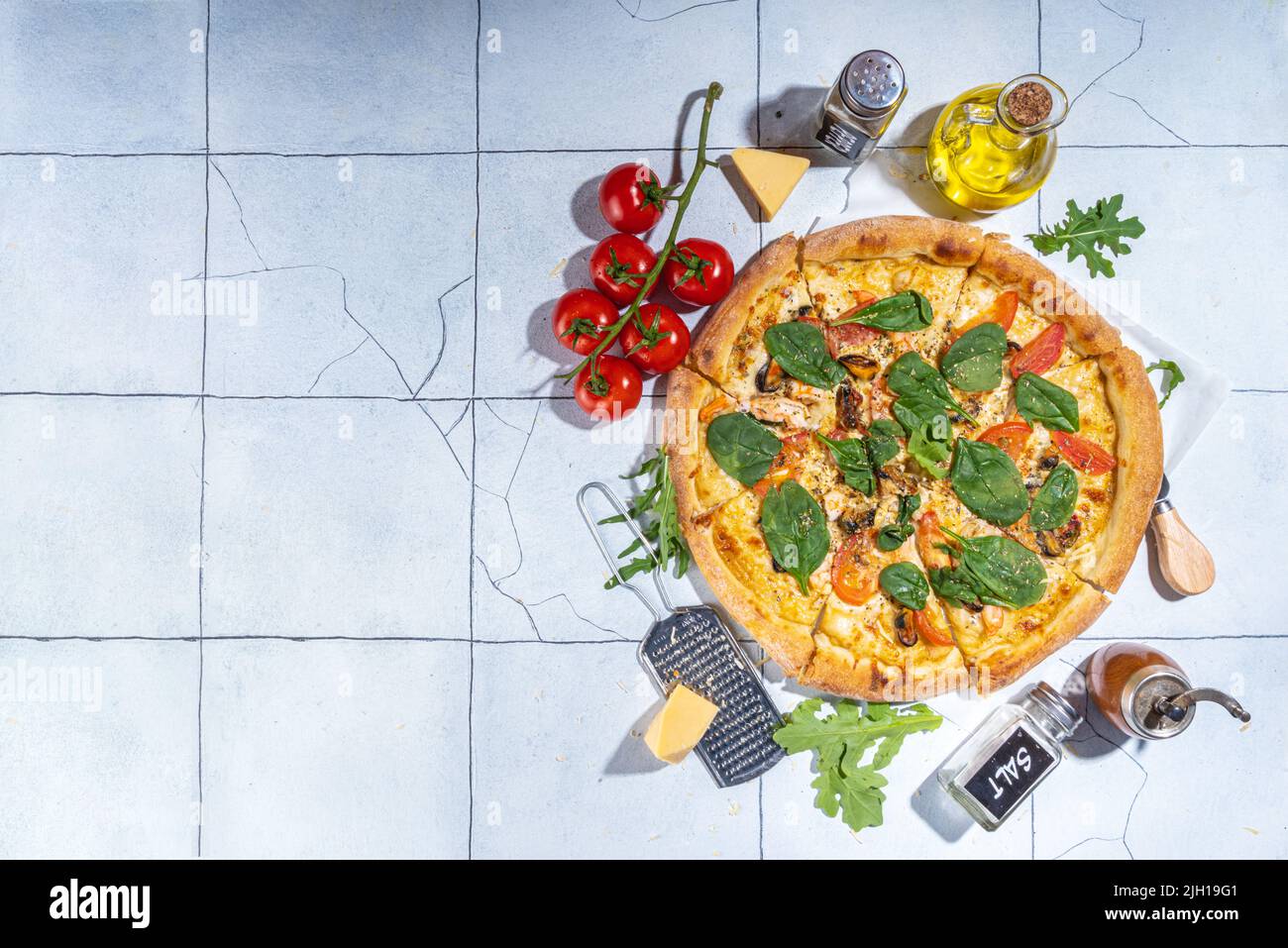 Three various pizzas, served at home or in restaurant on tiled table with cooking ingredients