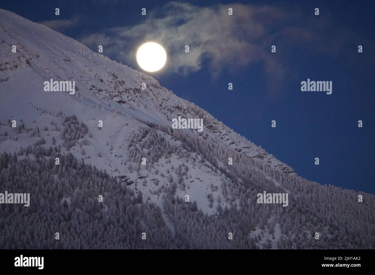 full moon rising on the mountains of the alps france on a clear cold snowy night Stock Photo