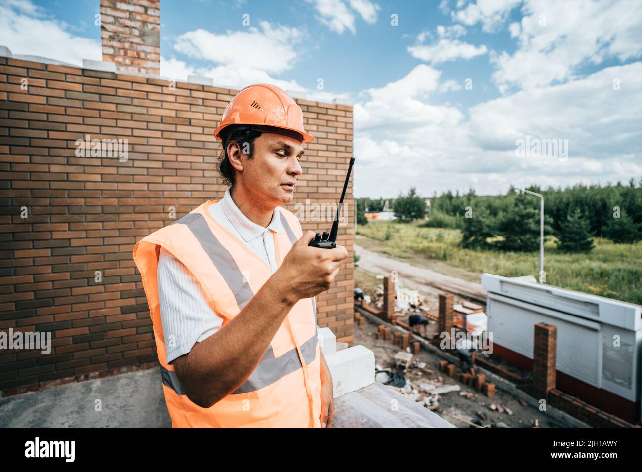 Foreman inspector or construction worker in hardhat portrait. Engineer in helmet with walkie-talkie in hand directs construction process. Stock Photo