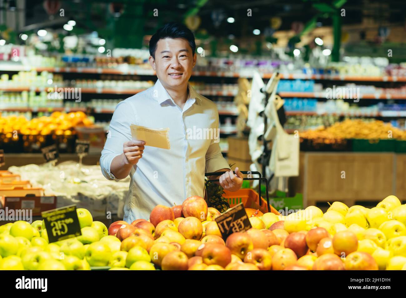 Asian man in supermarket chooses apple fruit, makes purchases looks at