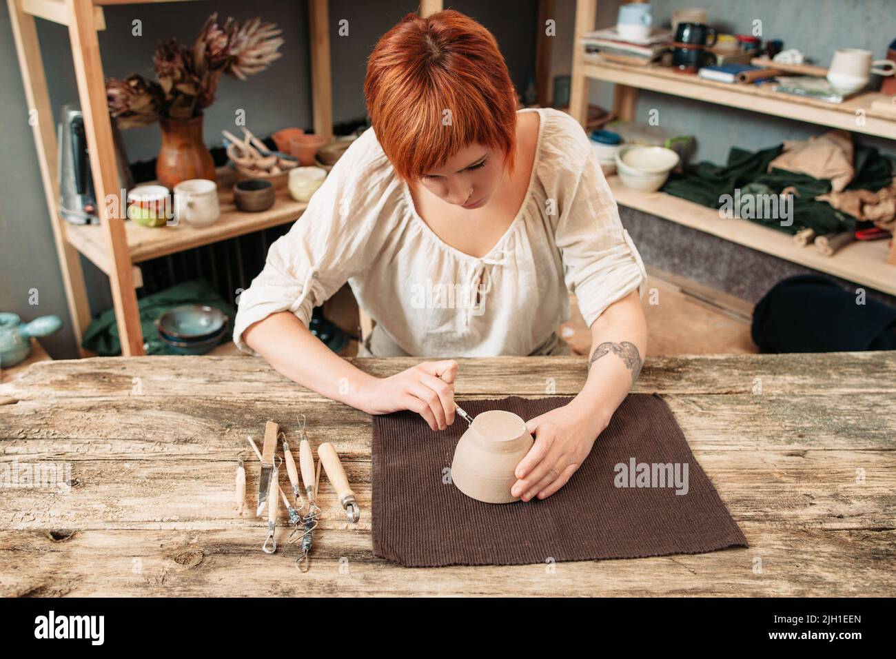 Female potter carving on pot, craftsman workshop Stock Photo