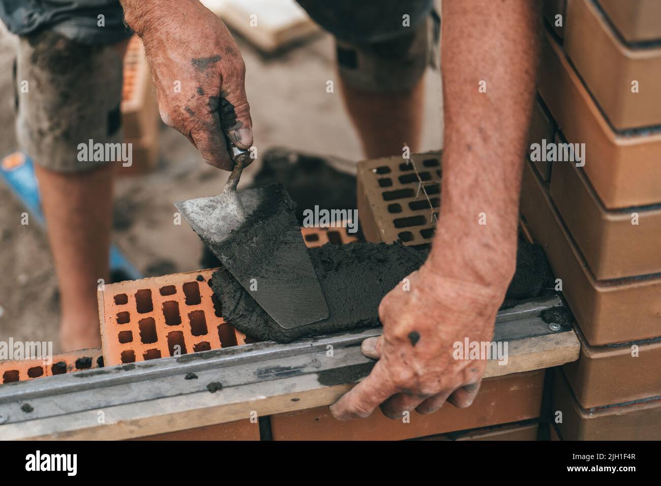Worker or bricklayer works with trowel laying bricks. Builder makes brickwork on construction site, close up on hands. Stock Photo