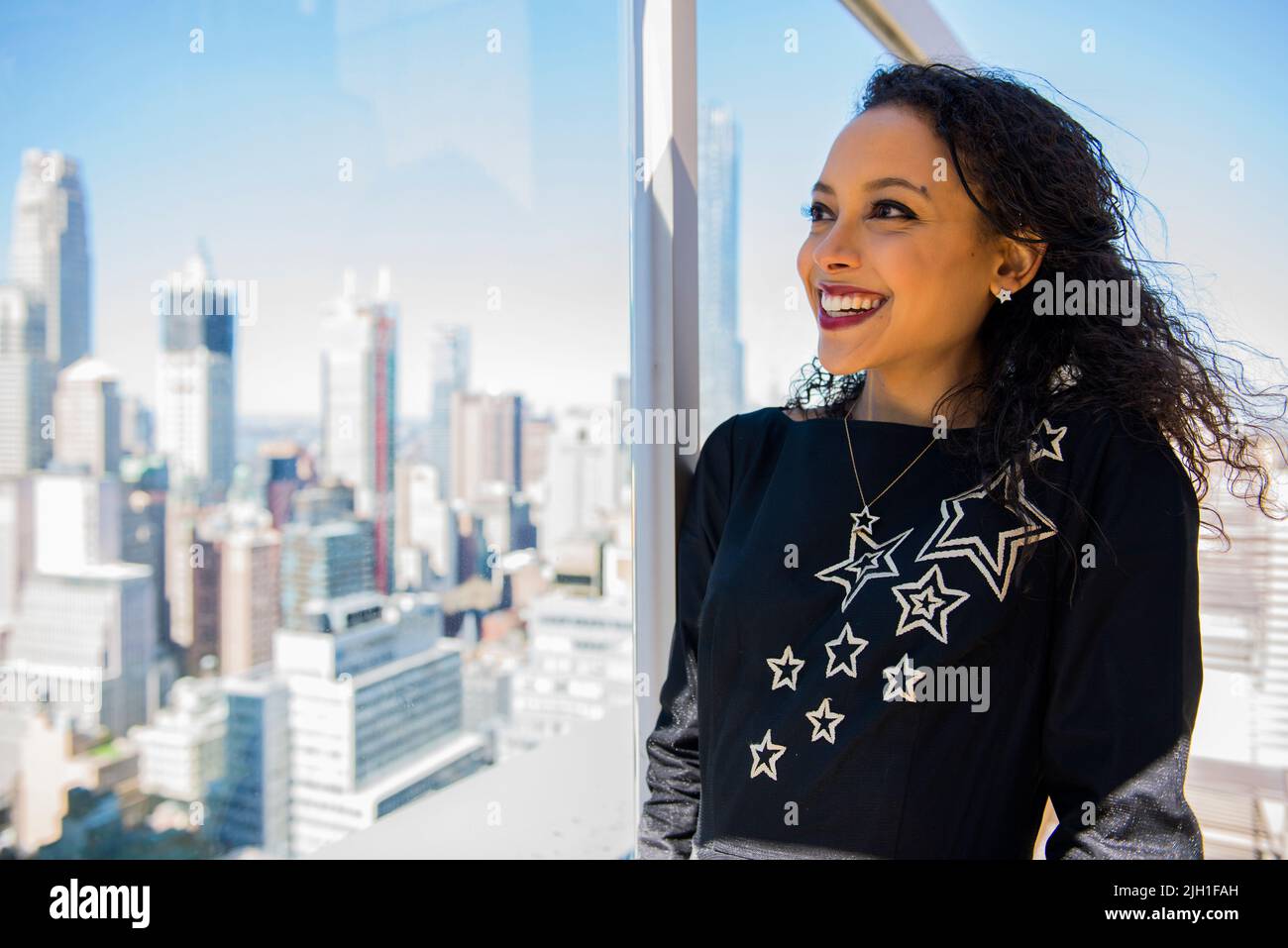 New York, USA. Attractive, Hispanic woman overlooking Down Town Manhattan Real Estate and Skyscrapers from the 58th floor of her apartment building. RealEstate is Booming in the Big Apple and usually very Expensive with Huge Competition on the Housing Market. Stock Photo