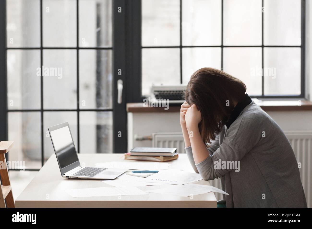 Tired business woman at workplace in office, holding her head in hands