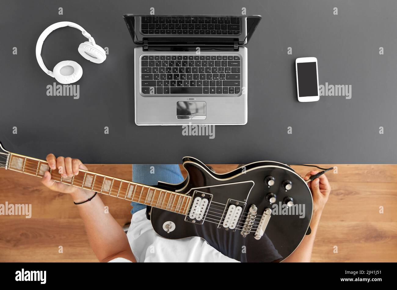 young man with laptop tuning guitar at table Stock Photo