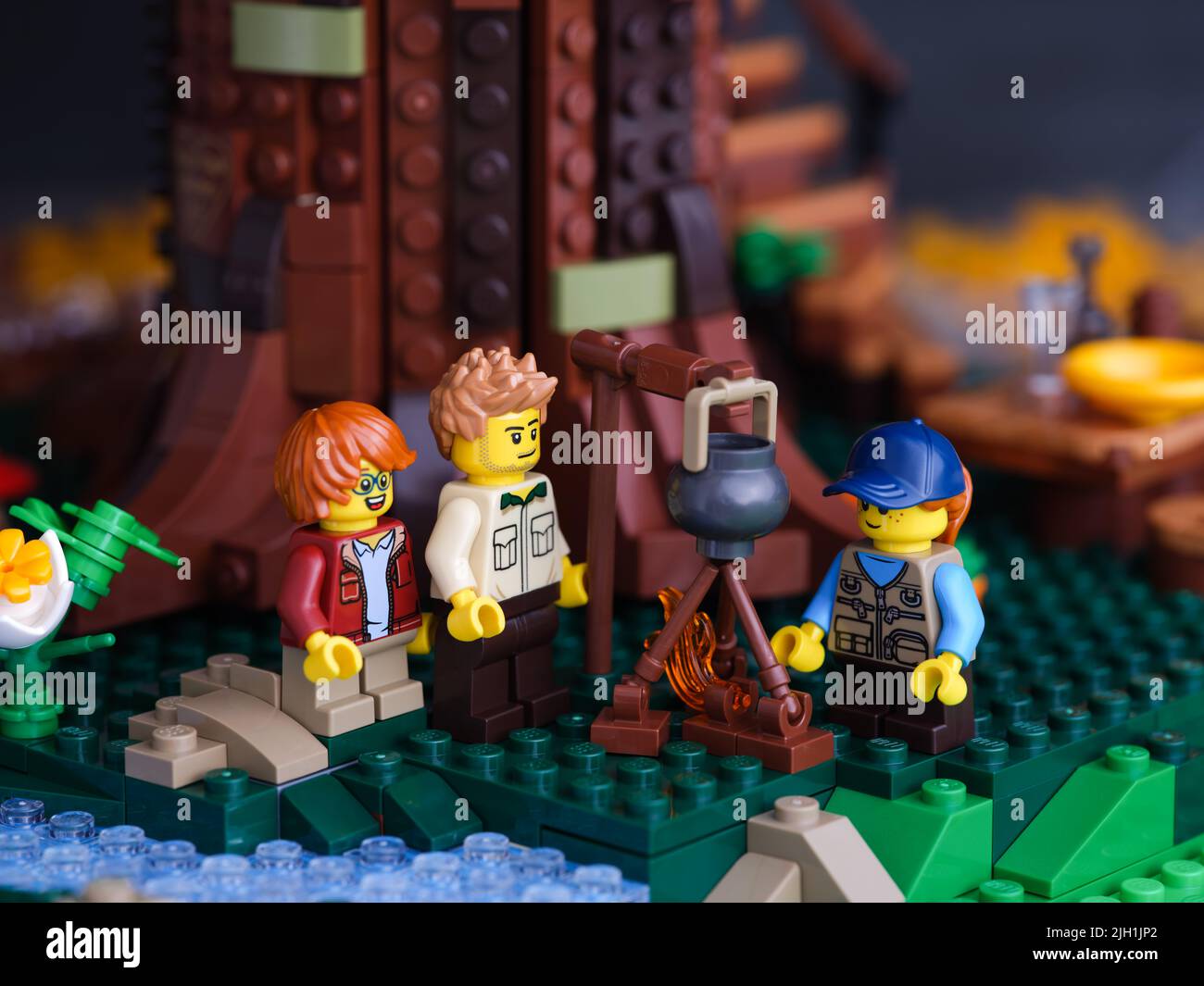 Tambov, Russian Federation - June 22, 2022  Three Lego minifigures - father and two children, standing under a tree and cooking food on a campfire. Stock Photo