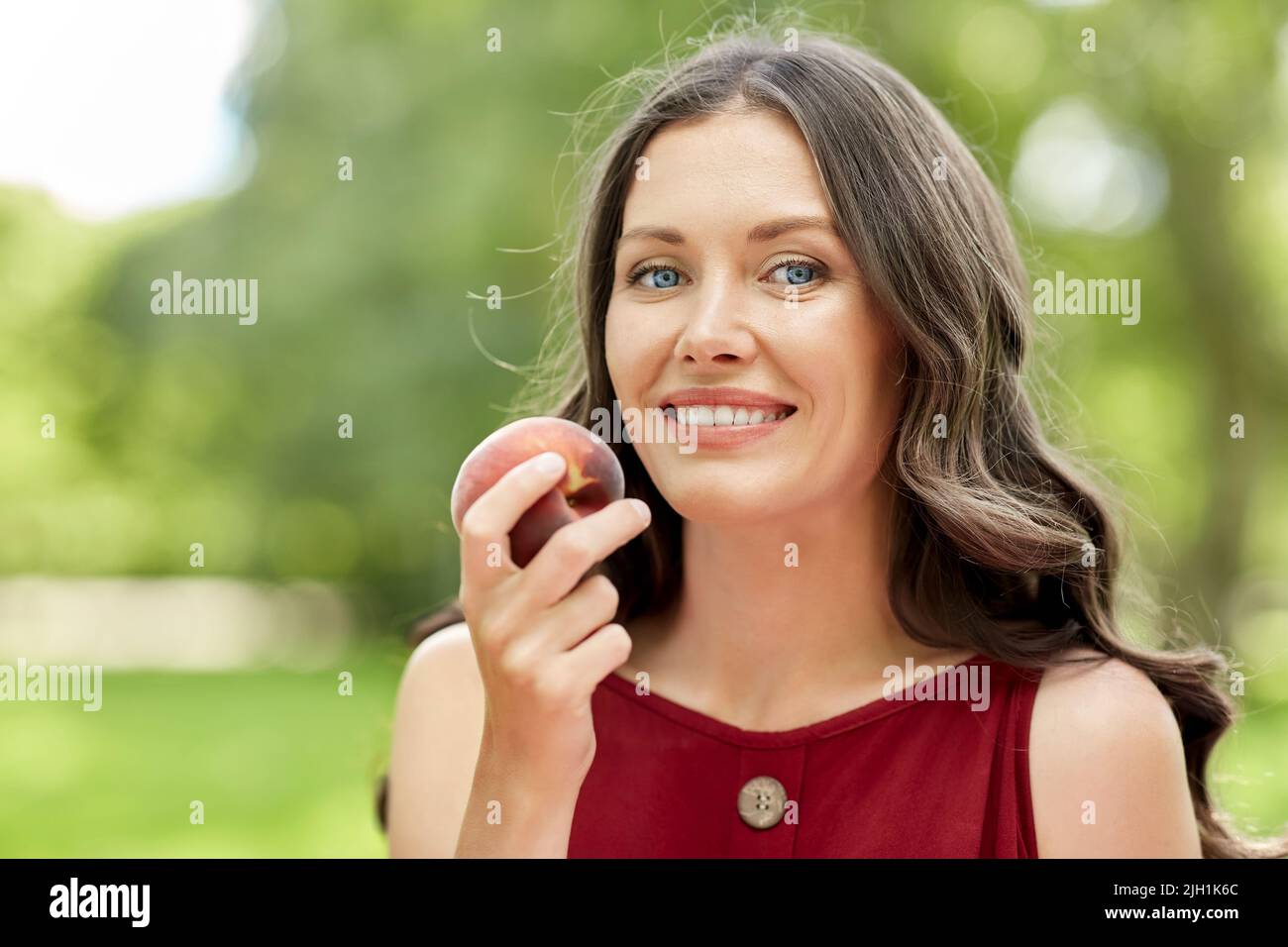 happy woman eating peach at summer park Stock Photo