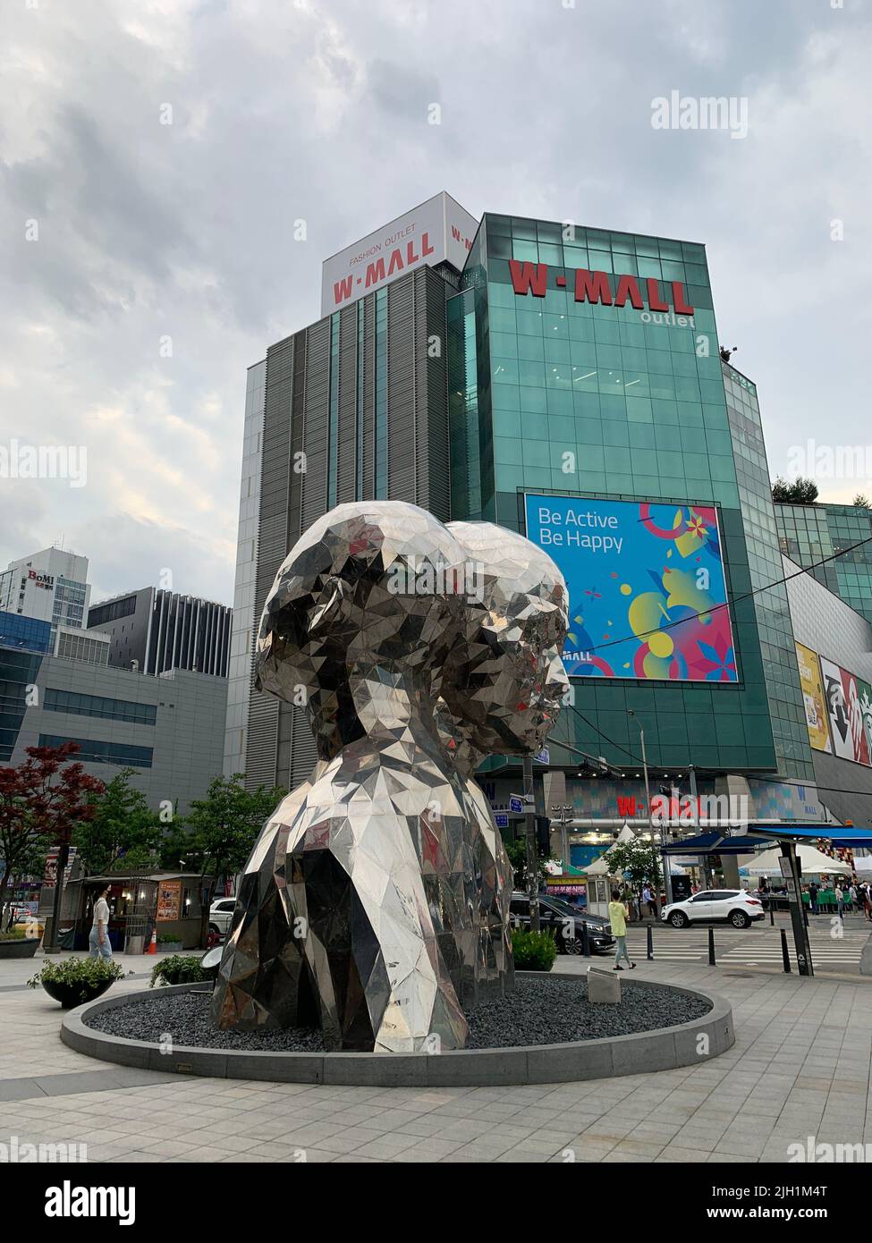A silver street art statue of two people with a mall in the background in Seul, South Korea Stock Photo