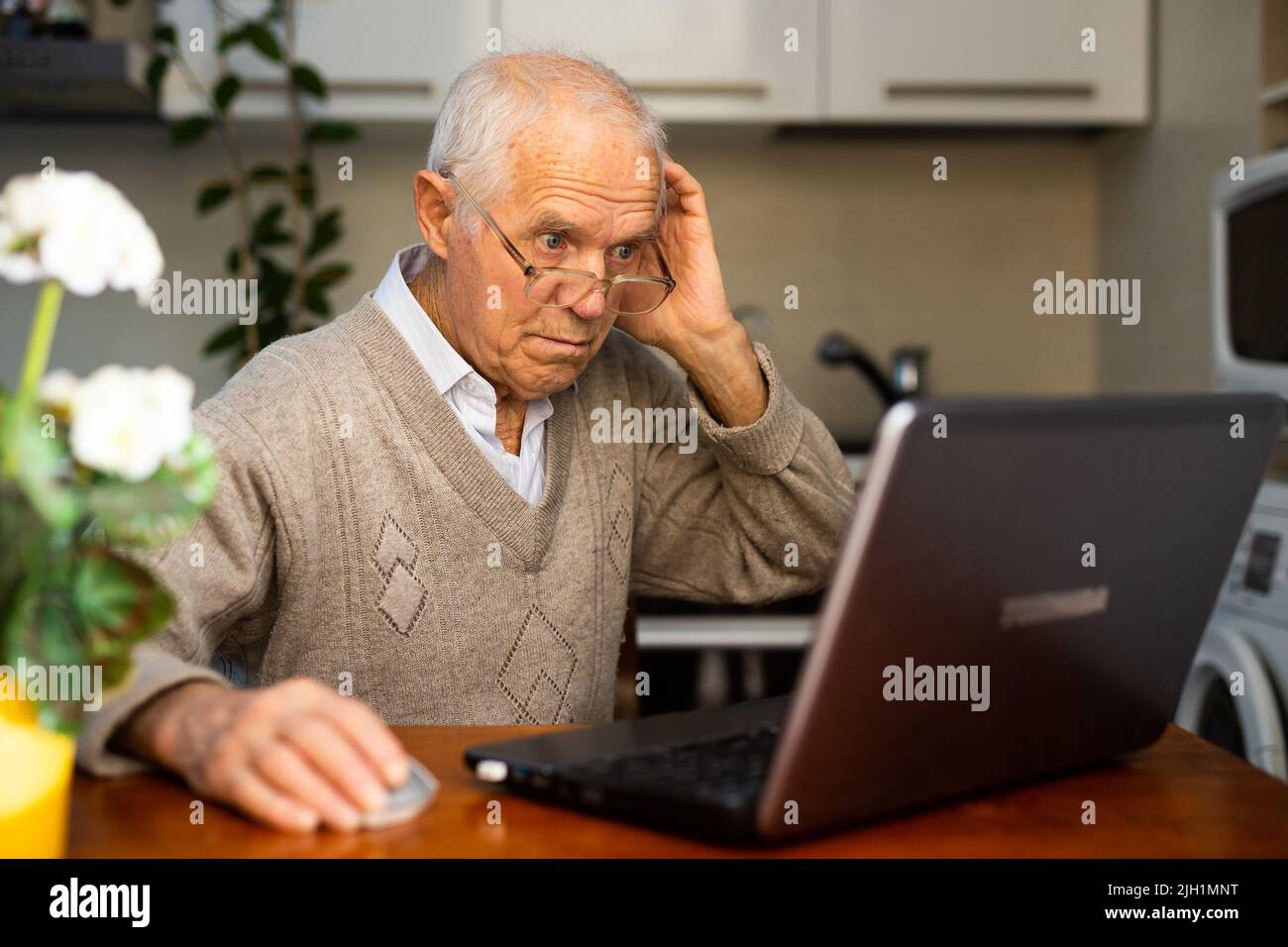 desperate old man pensioner chatting online via laptop with friends at home Stock Photo