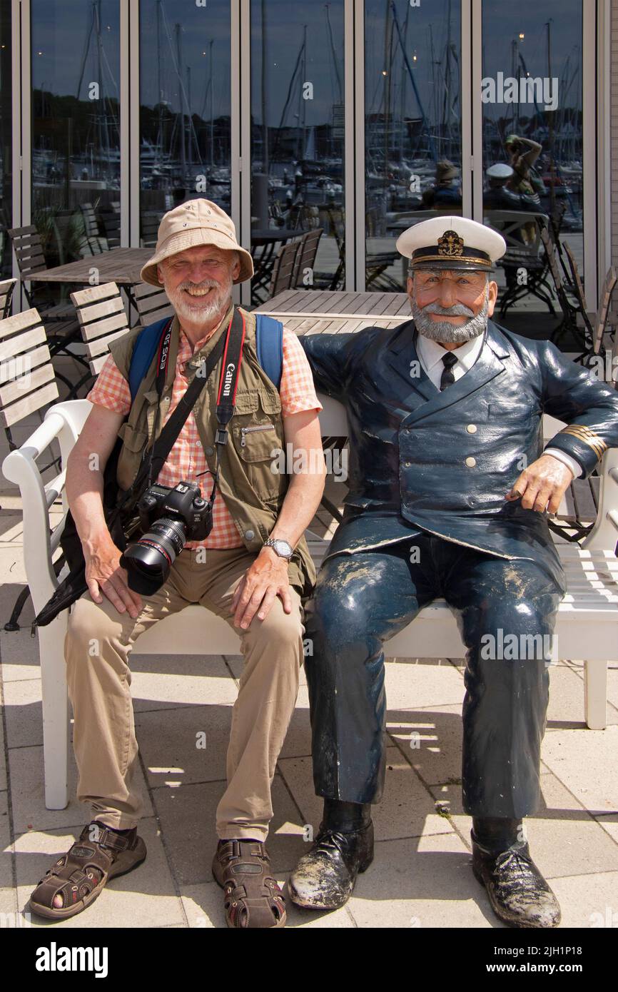 Elderly man sitting beside sculpture of a captain, Waterfront Quarter, Priwall, Travemünde, Lübeck, Schleswig-Holstein, Germany Stock Photo