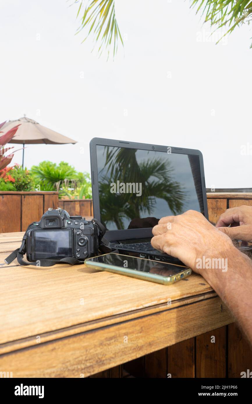 Close-up of a man working on a white-screen laptop computer on an old wooden table outside. Stock Photo