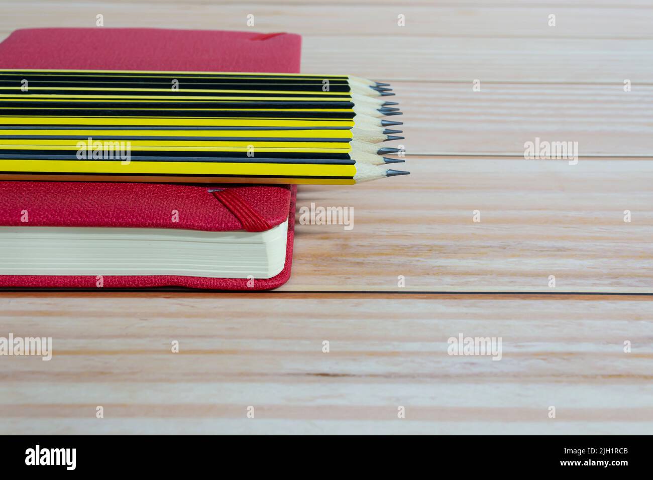 Wooden 2b pencils lying on red note book on wooden table. Copy space ...