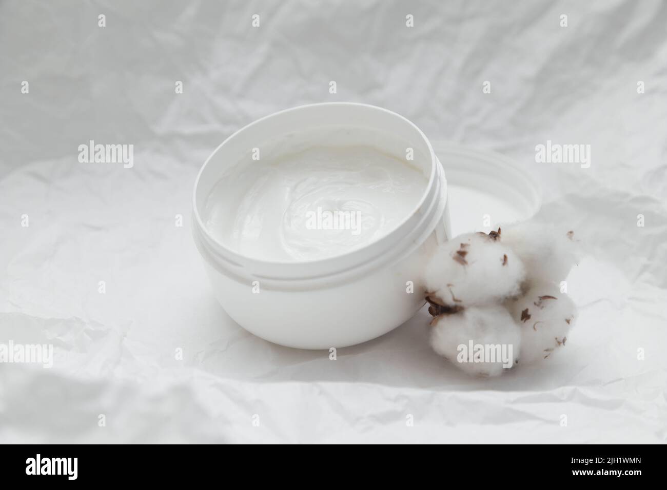 Cream in white opened plastic jar and cotton bud on white crumpled