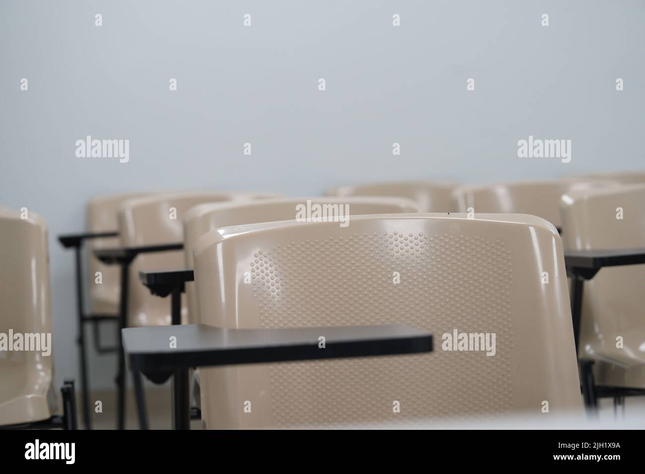 Empty class at university or school with chairs and side table and large board in the background. The chairs are arranged in rows. Stock Photo