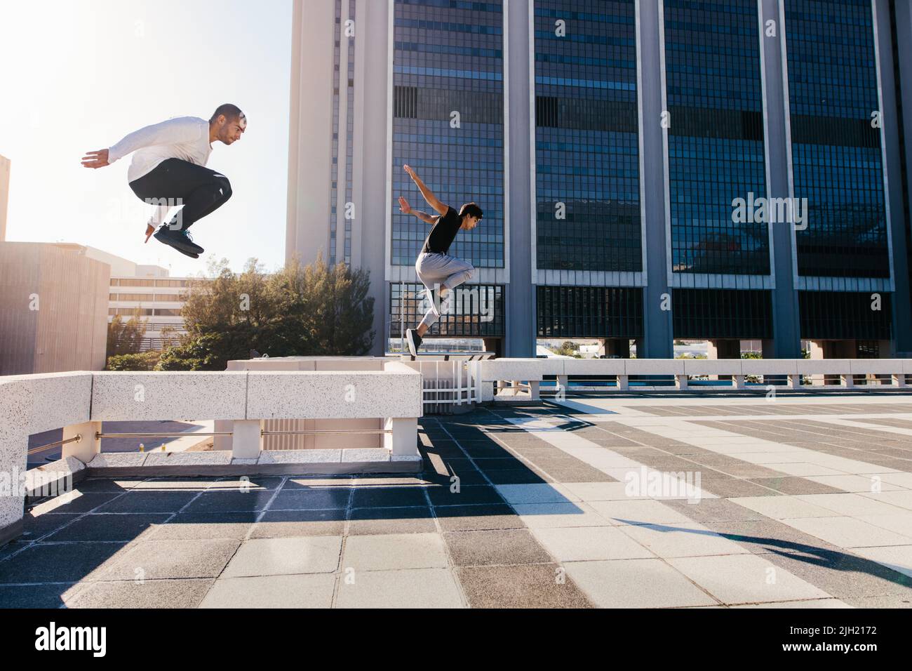 Two young sportsmen practicing parkour against a city background. Young people practicing extreme sport activities outdoors in city. Male athletes run Stock Photo