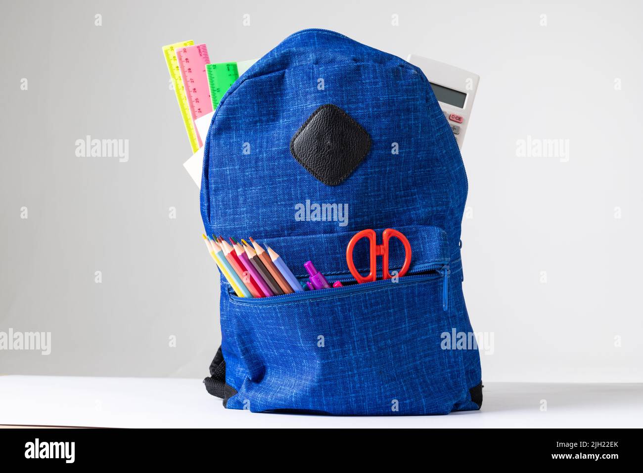 Vertical image of backpack with school equipment on white surface Stock Photo