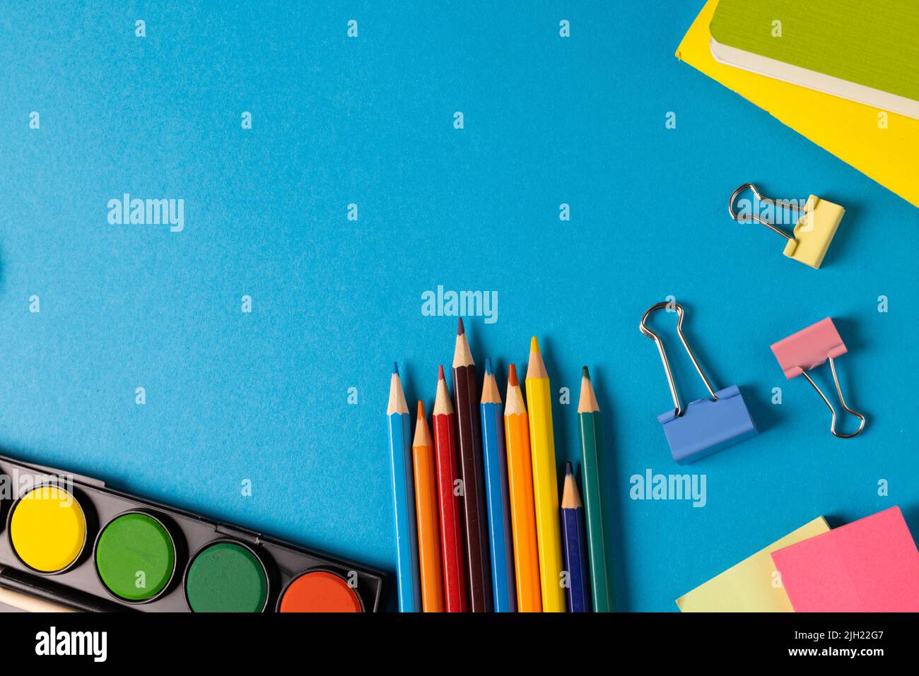 Composition of watercolors, crayons and clips on blue surface with copy space Stock Photo