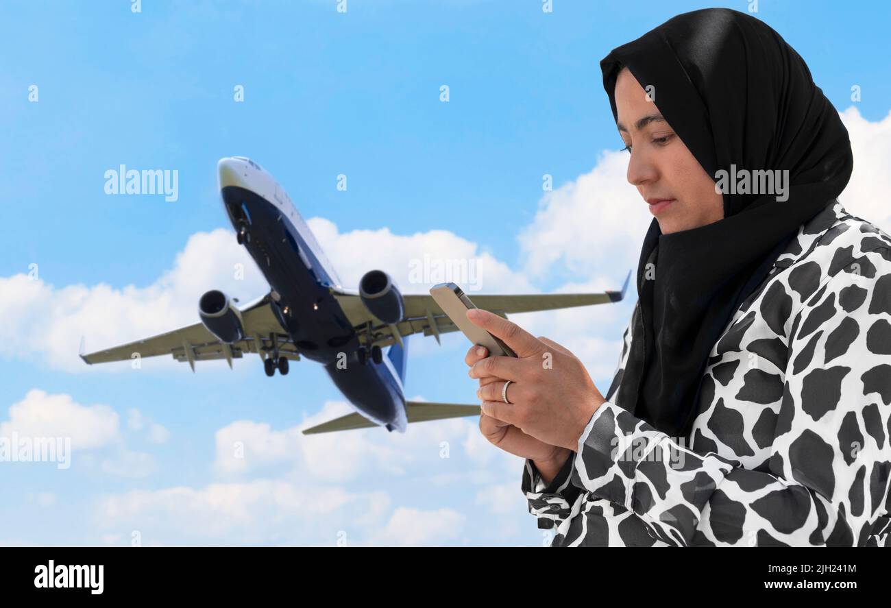 Muslim woman using her phone near a flying plane Stock Photo