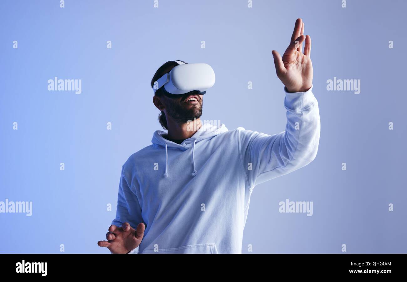 Happy young man touching virtual space with his hand. Cheerful young man experiencing a fun 3D simulation. Young man interacting with the metaverse us Stock Photo