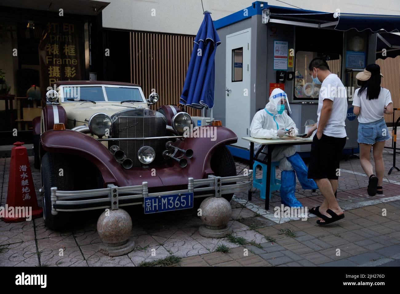 A pandemic prevention worker sits next to a vintage car as he scans a man's ID card at a nucleic acid testing station, amid a coronavirus disease (COVID-19) outbreak, in Beijing, China, July 14, 2022. REUTERS/Thomas Peter Stock Photo