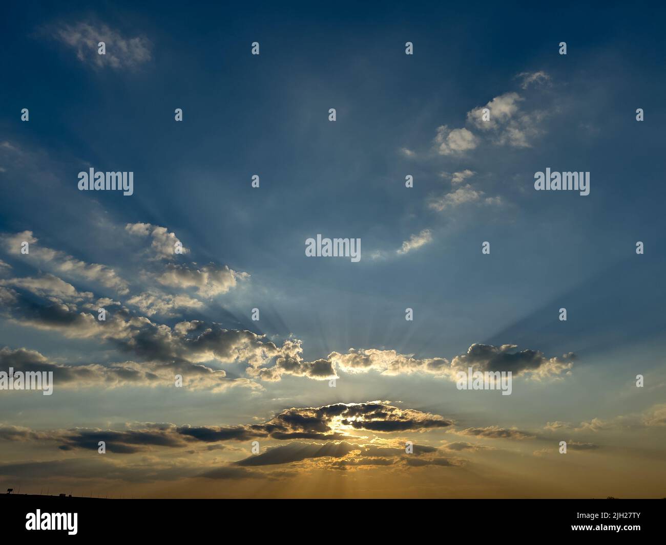 Dramatic sunset with rays and the sun behind the clouds. Stock Photo