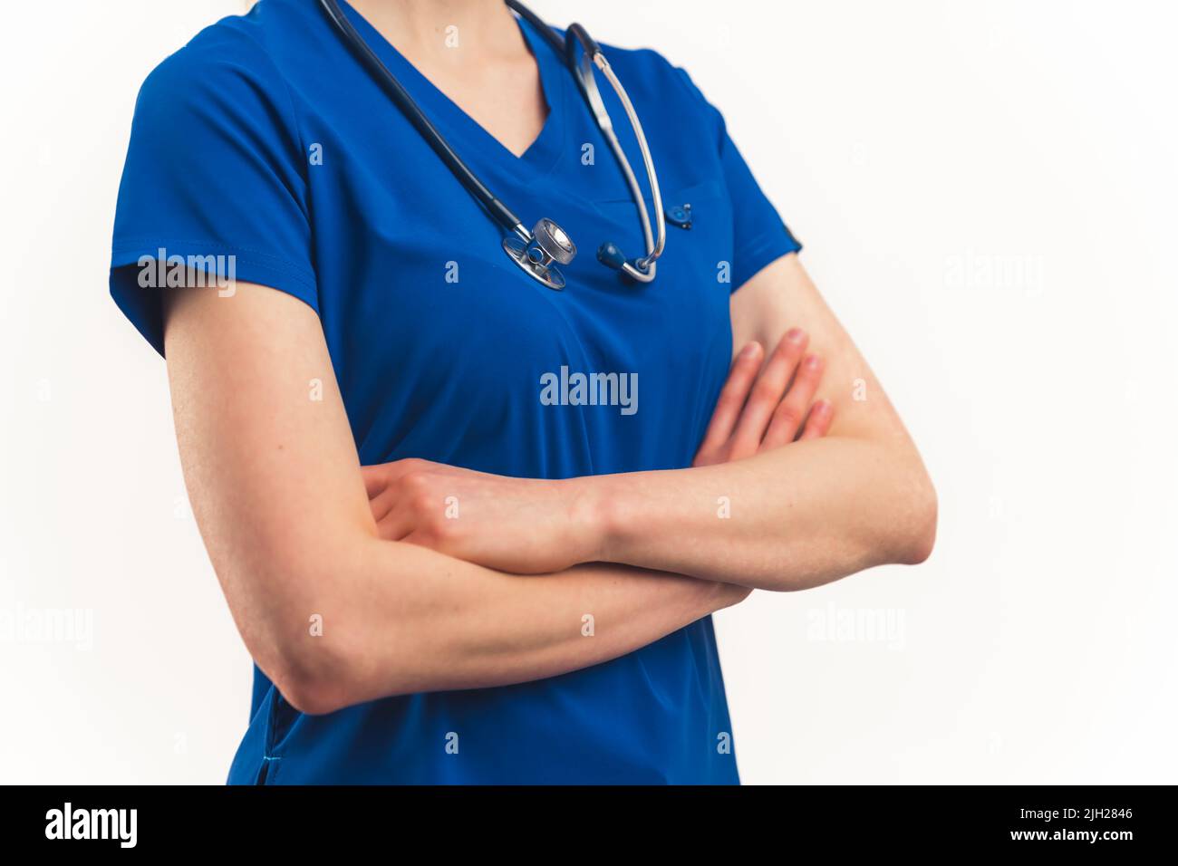 Unrecognizable middle shot of a caucasian person with crossed arms, wearing dark blue hospital nurse or doctor uniform with a stethoscope over neck. Isolated copy space white background studio shot. High quality photo Stock Photo