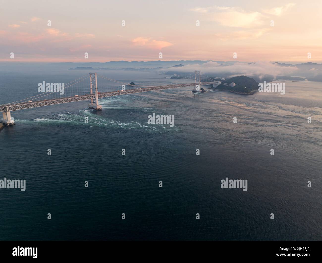 Strong tidal current flows under Naruto suspension bridge at sunset Stock Photo