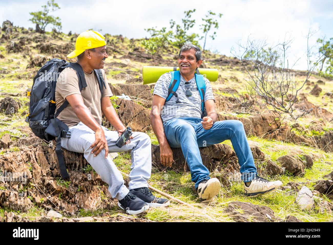 Happy smiling hikers talking each other during trekking for break while sitting on top of hill - concept of happiness, friendship and traveling. Stock Photo