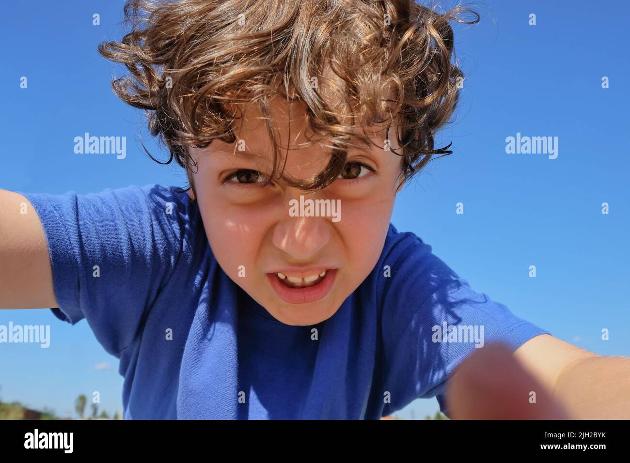 Selective focus to excited emotion face of arabian preschooler boy with big hazel eyes on blurred blue sky background. Portrait of irritated  boy Stock Photo
