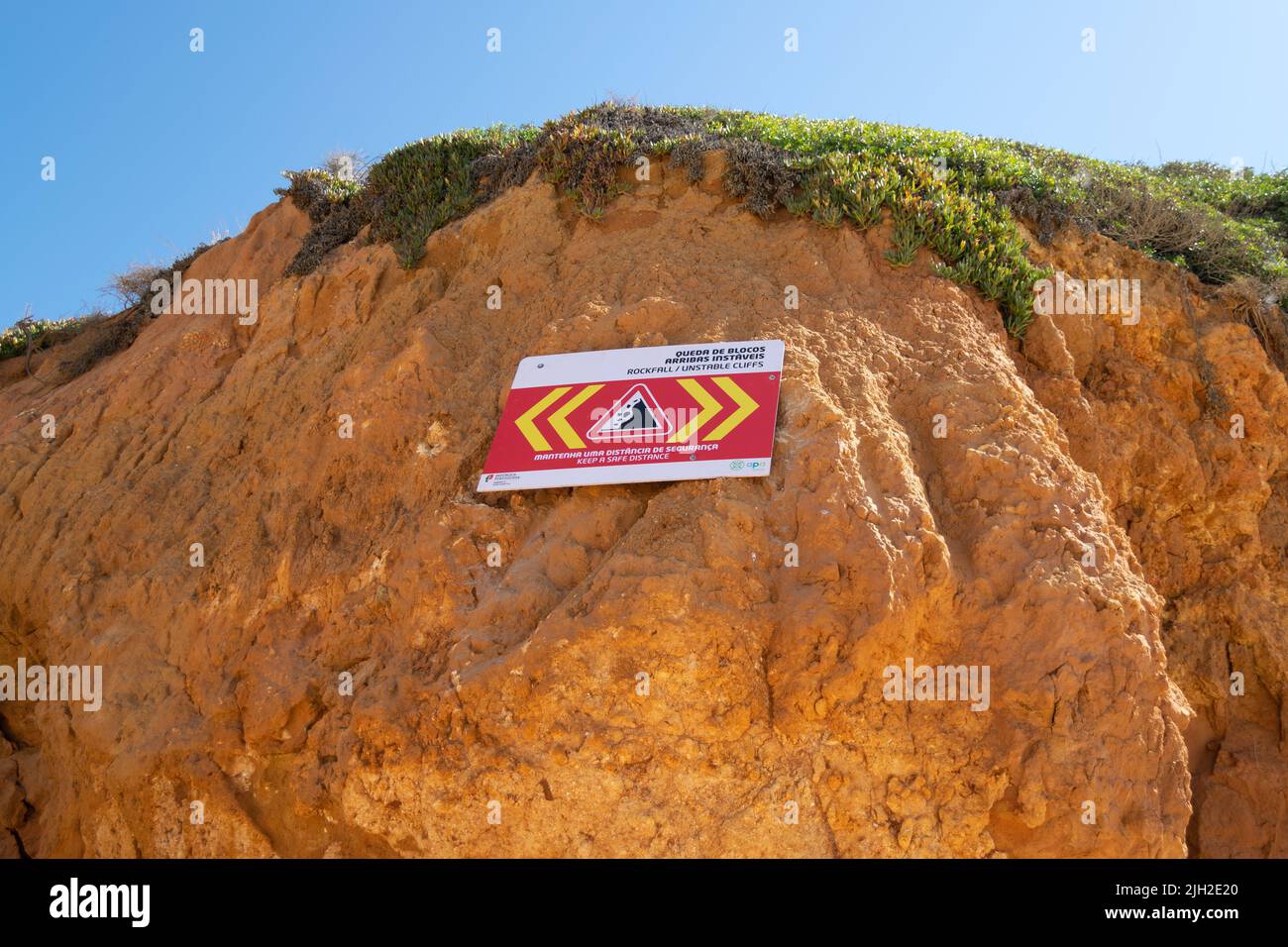 Cliffs rockfall signs in Algarve Portugal. Beach cliffs, rockfall zone on coastal beaches. Dangerous areas on beaches under cliffs. Cliff collapsing zone Stock Photo