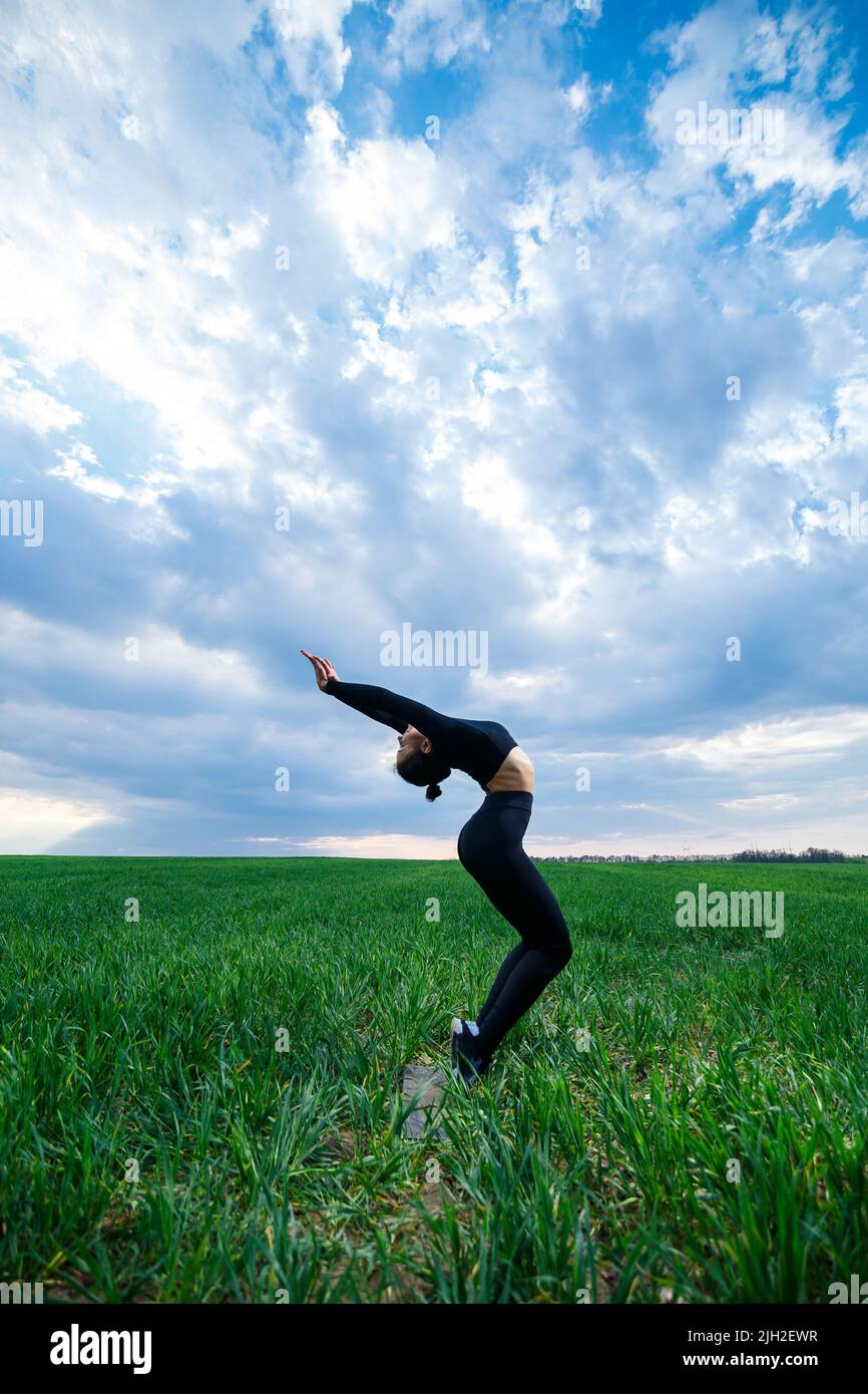 A beautiful brunette on a green lawn performs acrobatic elements Stock Photo