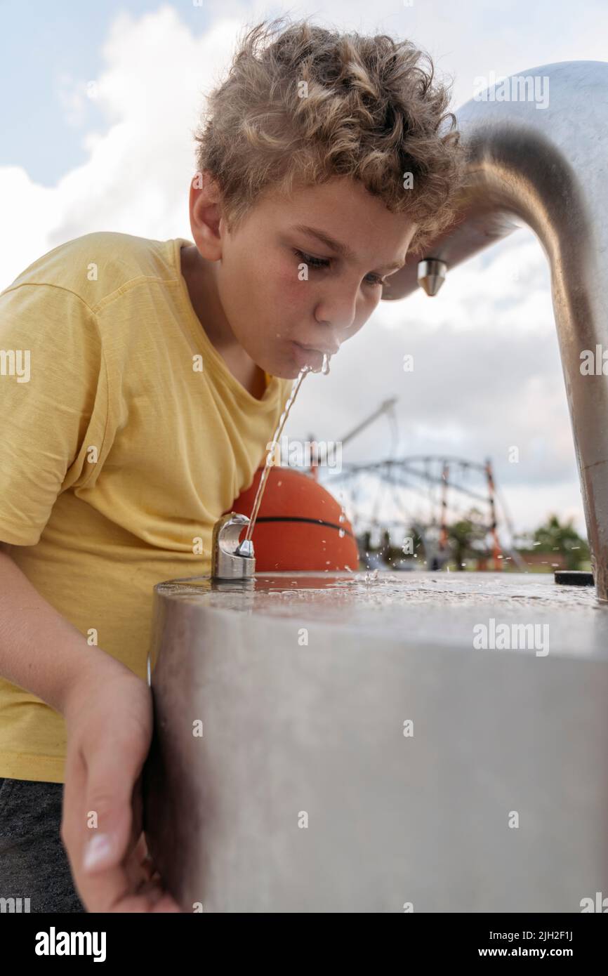 A boy with a basketball drinks water after a workout. Stock Photo