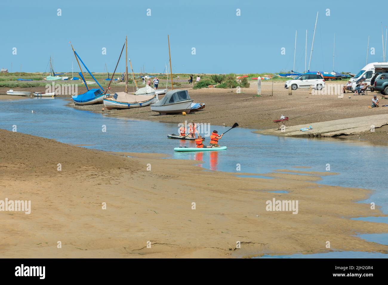 Children summer, view of children paddling across the shallow River Glaven at low tide in the scenic harbour in Blakeney, north Norfolk coast, England Stock Photo