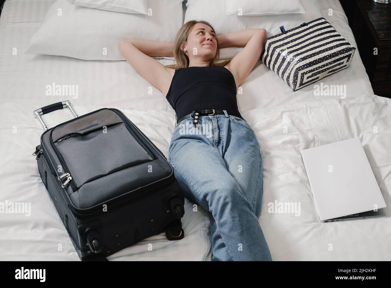 Woman with suitcase on bed in hotel having rest while traveling. Relaxed happy Traveler with bags in hostel Top view. Enjoying trip booking apartments Stock Photo
