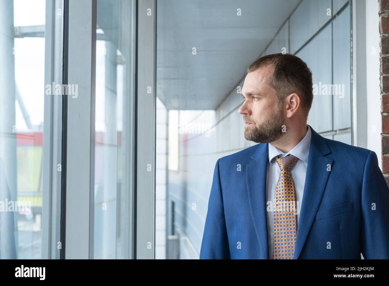 A smart, serious, confident Arab businessman looking out the window at the street. Portrait of a handsome middle-aged businessman in a suit. The conce Stock Photo